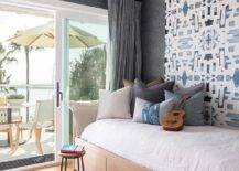 Charcoal gray curtains cover sliding glass doors surrounded by charcoal gray wallpaper in a bedroom featuring a custom built daybed fitted with drawers and mounted against an accent wall clad in blue trellis wallpaper. The bed sits on a blue jute rug.