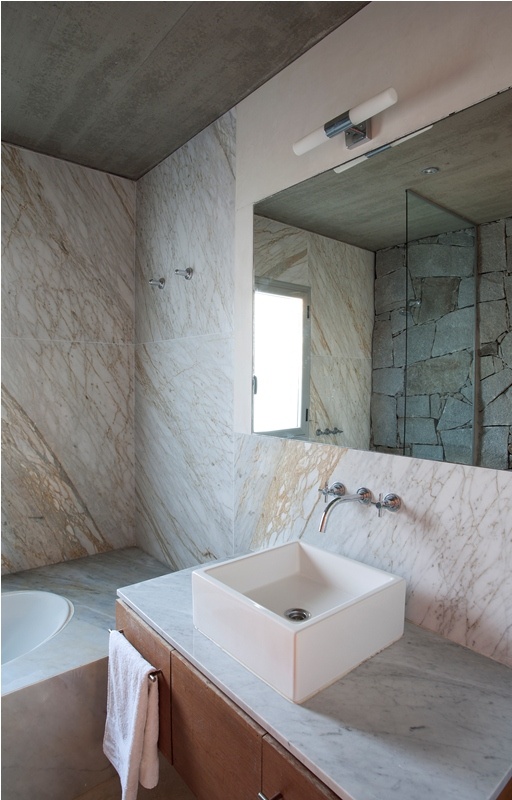A large bathroom featuring marble walls and a generously sized mirror reflecting the room's ambiance which is mounted above a wood vanity.
