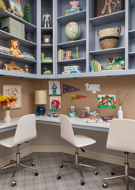 Blue built-in shelves are mounted over a pinboard backsplash lining an l-shaped blue built-in desk with a white top seating white task chairs on a gray tiled floor.